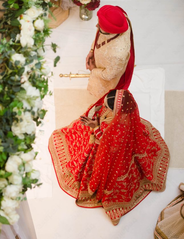South Asian Bride in red lehenga and groom in ivory sherwani posing side by side.
