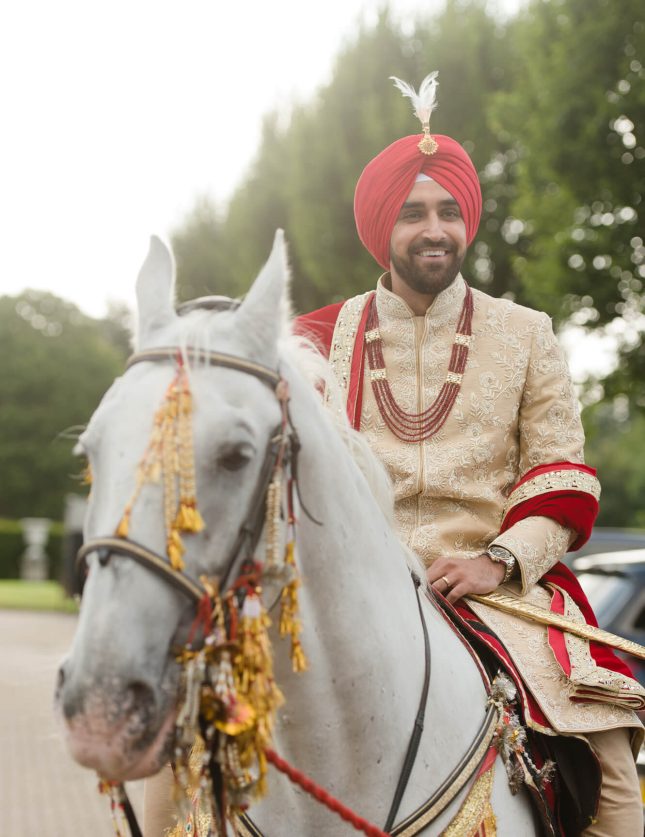 Groom in traditional cream South Asian Wedding Outfit entering Hedsor House on horse back