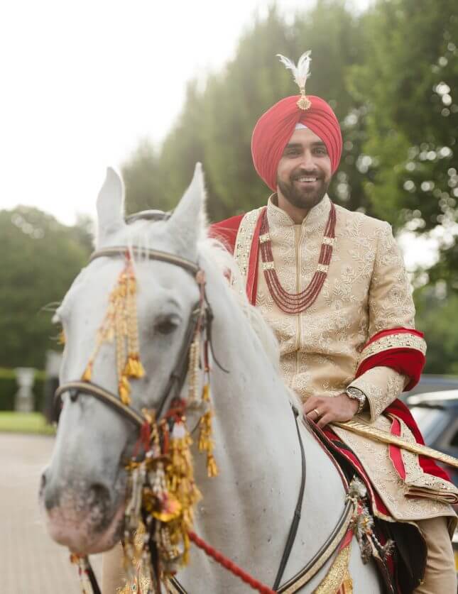 Groom in traditional cream South Asian Wedding Outfit entering Hedsor House on horse back