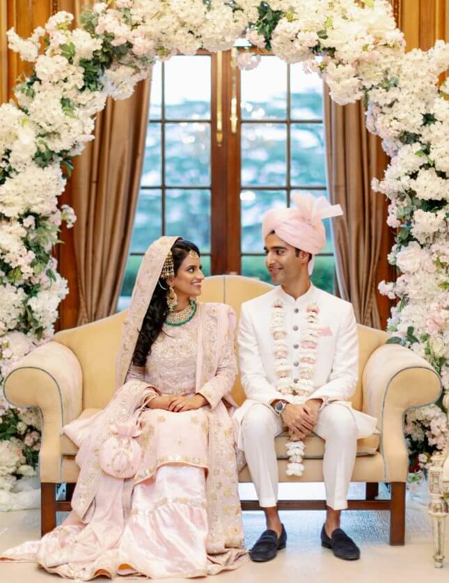 Bride and groom sat under a floral display at their traditional south Asian wedding ceremony